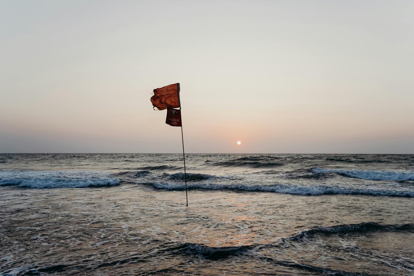 A red flag waves on a tranquil Goan beach at sunset, overlooking the serene ocean.